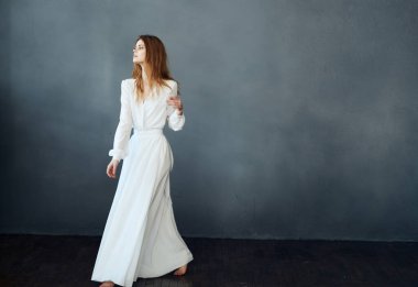 Beyaz elbiseli, kızıl saçlı bir kadın. Gri bir arka planda.