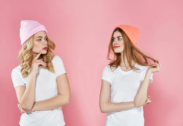 Duas namoradas bonitos vestindo camisetas chapéus de moda comunicação estilo de vida fundo rosa — Fotografia de Stock