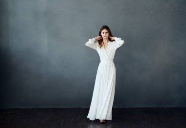 Beyaz elbiseli hoş bir bayan arka planda dans ediyor. El modeliyle el kol hareketi yapıyor.