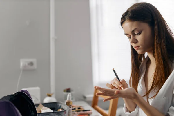 Kvinna som håller en penna och sitter vid bordet kosmetika eyeliner porträtt stiftelse — Stockfoto