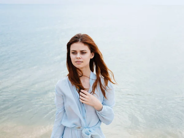 Une femme voyage sur la plage près de la mer avec une chemise bleue aux cheveux roux — Photo