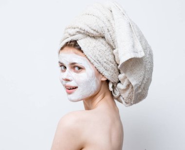 Bir kadın görünüşüne önem verir ve kafasında bir havlu ve yüzünde bir nemlendirici.