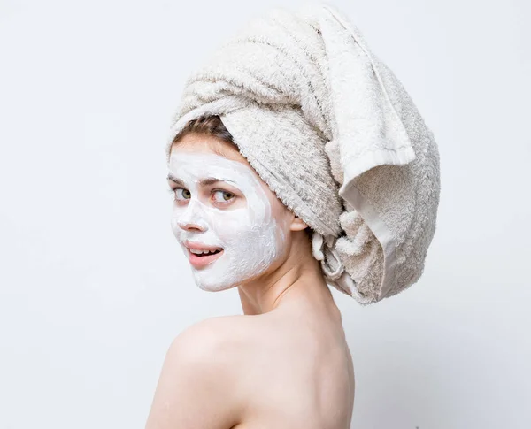 A woman cares for her appearance and a towel on her head and a moisturizer on her face — Stock Photo, Image