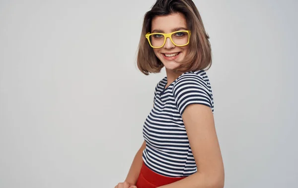 Mulher na moda em óculos e em uma camiseta listrada em um fundo leve saia vermelha — Fotografia de Stock