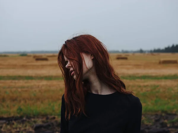 Portrait d'une femme aux cheveux roux vêtue d'une robe noire dans un champ en pleine nature vue dégagée — Photo