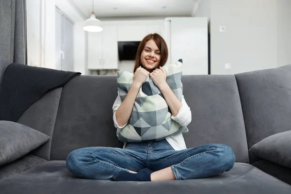彼女の手に枕を持つ陽気な女性はソファの上に座って残りのアパートのインテリア — ストック写真
