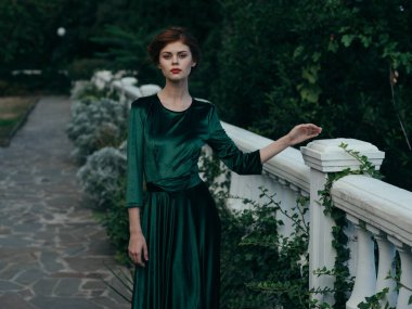 Yeşil elbiseli, yeşil ağaçlar üzerinde yürüyor. Lüks, zarif bir tarzı var.