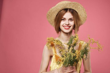 Mimoza çiçekli şapka buketi takan bir kadın.