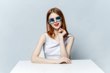 Gözlüklü kadın beyaz bir masada oturuyor. Duygular çekici görünüyor.