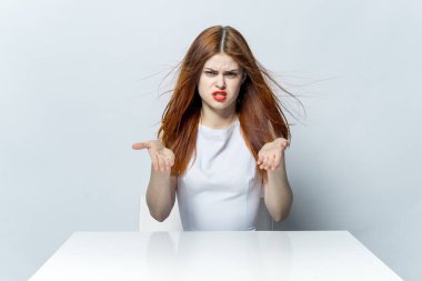 Güzel bir kadın masada oturmuş, elleri kırmızı dudaklarıyla el kol hareketi yapıyor.