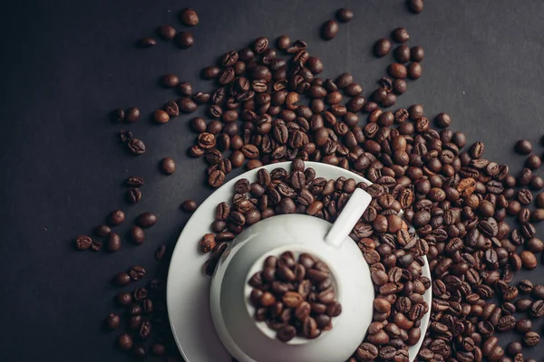 Taza blanca y platillo y granos de café grandes sobre un fondo oscuro macro fotografía — Foto de Stock