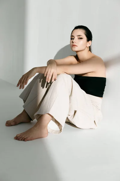 Mulher descalça em roupas da moda senta-se no chão em um quarto brilhante — Fotografia de Stock