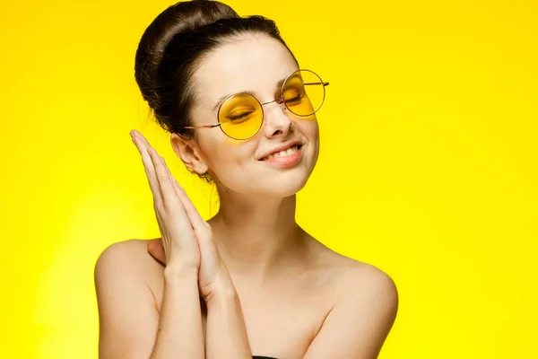 Эмоциональная женщина с обнаженными плечами в модных очках собрала волосы на желтом фоне — стоковое фото
