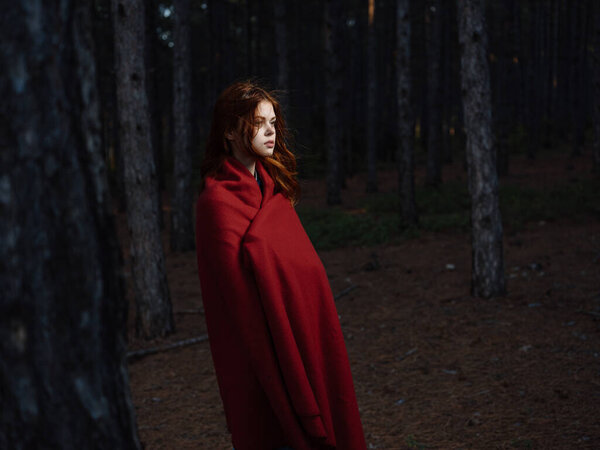 A red-haired woman with a plaid on her shoulders walks in the forest near the trees. High quality photo