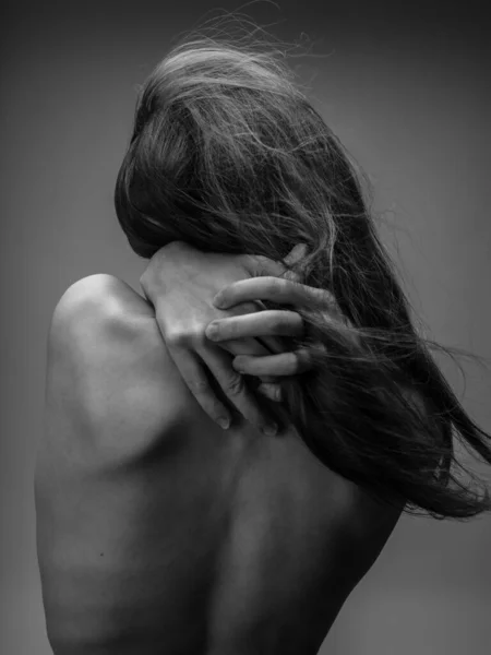 De vrouw op de grijze foto raakt zichzelf aan met haar blote rug. — Stockfoto