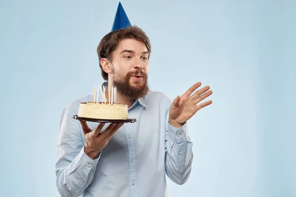 Pastel en un plato y hombre de cumpleaños con una gorra en su cabeza fondo azul — Foto de Stock