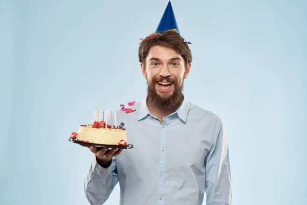Hombre con un plato de pastel y una vela festiva fondo azul gorra fiesta corporativa — Foto de Stock