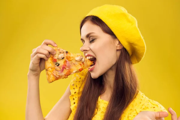 Mulher de chapéu amarelo com um pedaço de pizza em suas mãos em um fundo amarelo corte vista de modelo de emoção — Fotografia de Stock