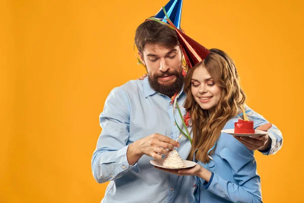 Muž a žena na party v čepicích a s tinsel dort zábava žluté pozadí — Stock fotografie