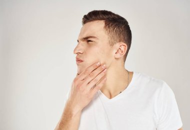 Hafif arka planda bir adam elleriyle yüzüne dokunuyor ve beyaz bir tişört mankeni