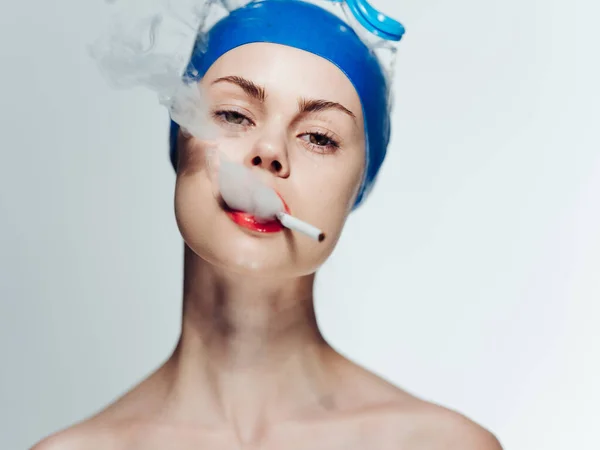 Una mujer con gorra azul fuma sobre un fondo claro con un cigarrillo en los dientes — Foto de Stock