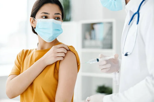 En patient på sjukhus och en läkare i skyddshandskar injicerar ett vaccin i axeln på en kvinna som — Stockfoto