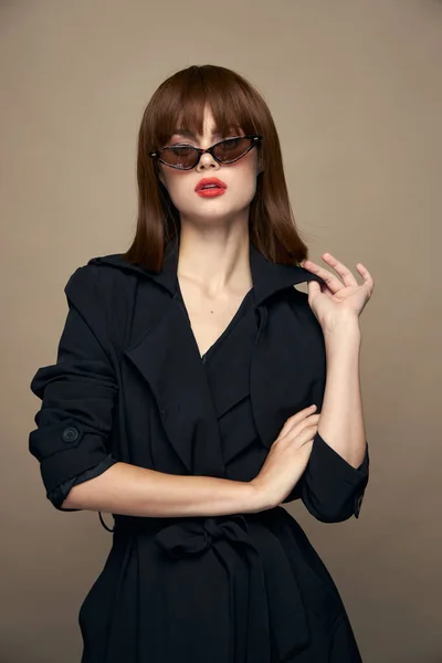 Stijlvolle vrouw zonnebril beige achtergrond zwart jas — Stockfoto