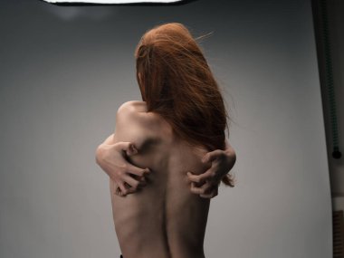 Çıplak kadın elleriyle arkasına dokunuyor duygularını geriyor kızıl saçlarını.