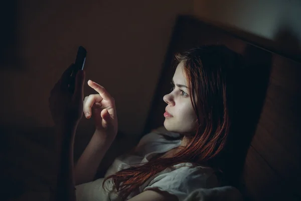 ผู้หญิงในห้องนอนนอนกับโทรศัพท์ในมือเธอเสพติด — ภาพถ่ายสต็อก