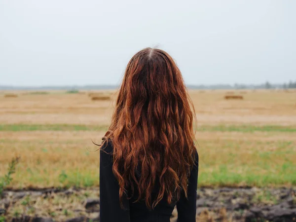 Mulher bonita com cabelo vermelho em um vestido preto ao ar livre no campo — Fotografia de Stock