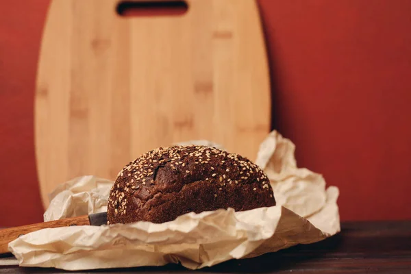 Pan oscuro de centeno con un cuchillo en un paquete de papel imagen de textura de mesa de madera —  Fotos de Stock