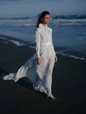 Okyanus kenarındaki beyaz elbiseli kadın çıplak ayaklı portresi.