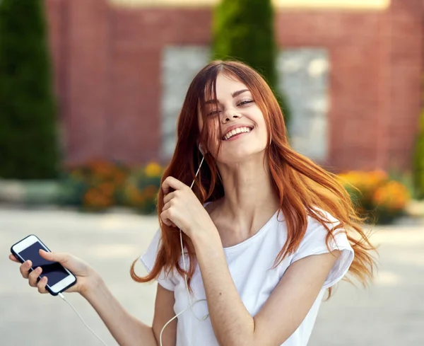 Woman in a white t-shirt on the street music with headphones walking — Stock Photo, Image