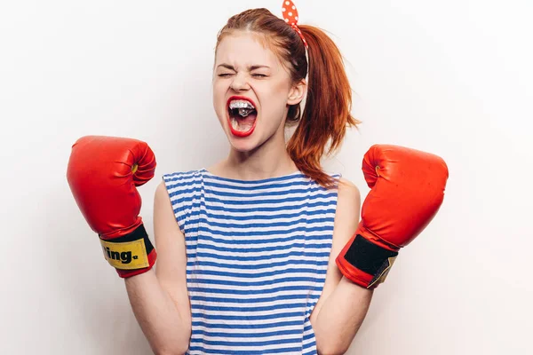 Rothaarige Frau in Boxhandschuhen und gestreiftem T-Shirt vor hellem Hintergrund mit offenem Mund — Stockfoto