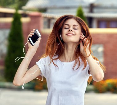 Beyaz tişörtlü neşeli bir kadın sokak müziğinde kulaklık takıyor.