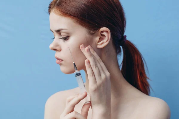Kvinna som håller sprutan nära ansiktet botox föryngring injektion blå bakgrund — Stockfoto