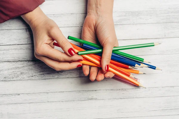 Lápices de colores brillantes en manos femeninas fondo de madera textura gris — Foto de Stock