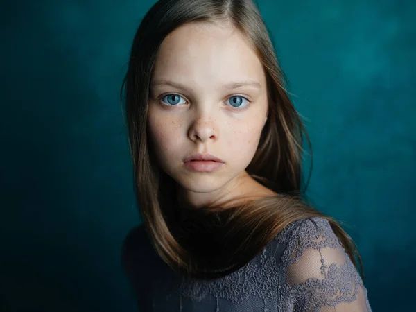 Retrato de una hermosa niña con un vestido gris sobre un fondo turquesa y ojos azules — Foto de Stock