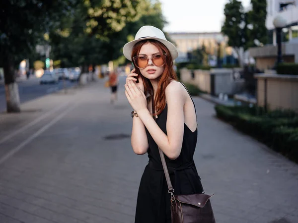 Ładna kobieta w sukience i kapeluszu z torbą na ramieniu idzie ulicą. — Zdjęcie stockowe