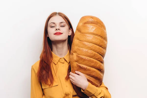 Large loaf of bread loaf in the hand of a woman in a yellow shirt on a light background — Stock Photo, Image