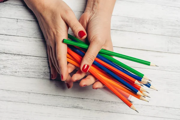 Helder gekleurde potloden in vrouw handen op houten achtergrond bijgesneden uitzicht — Stockfoto