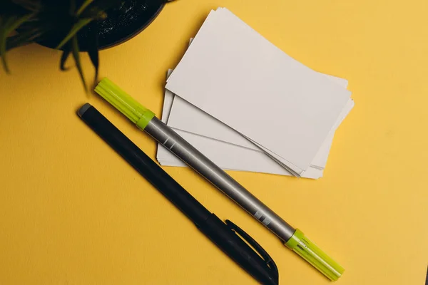 markers pens and rubber bands on a yellow background flowers in a pot and a cup of coffee