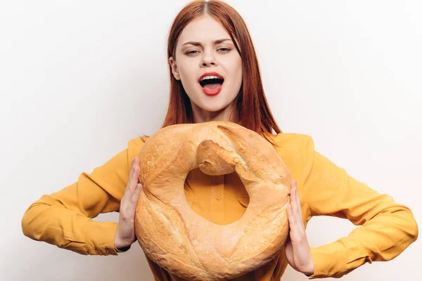 Uma jovem mulher segura um pão redondo em suas mãos em um fundo leve em uma camisa amarela — Fotografia de Stock