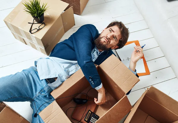 A man with boxes lies on the floor of an office moving room unpacking