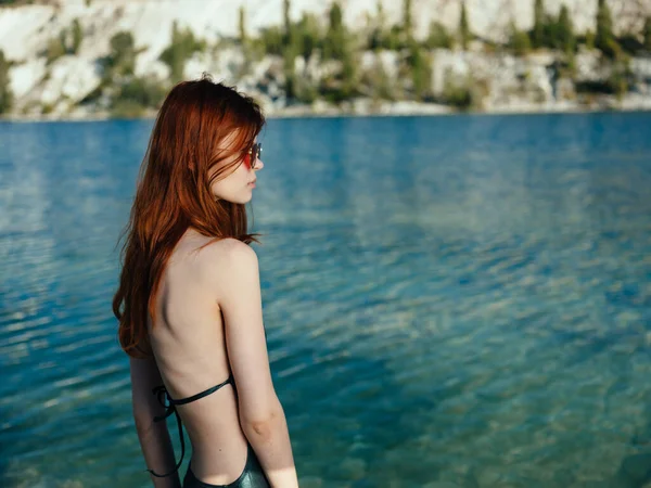 Red-haired woman in sunglasses and in a green swimsuit near the river — Stock Photo, Image