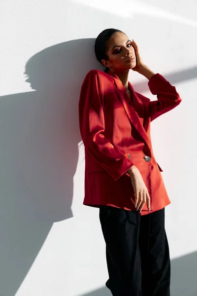 Mulher na moda em uma jaqueta vermelha e calças pretas segurando a mão acima da cabeça Em um quarto brilhante — Fotografia de Stock