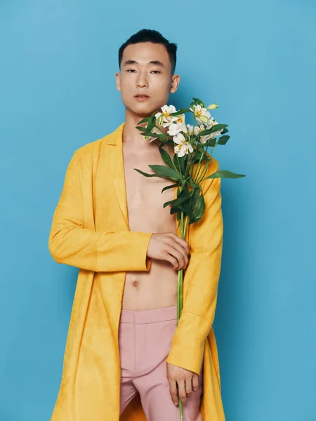 Homem sexy com um tronco nu e em um casaco amarelo segurando um buquê de flores em sua mão — Fotografia de Stock