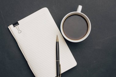 Koyu arka planda kalem ve bir fincan kahve ofisi manzaralı defter.