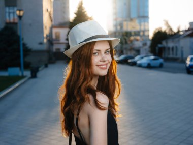 Şehrin caddesinde siyah elbiseli, beyaz şapkalı, kızıl saçlı bir manken.