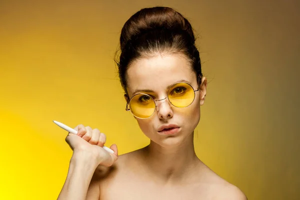 Brunette in yellow glasses naked shoulders cigarette in hands emotions yellow background — Stock Photo, Image